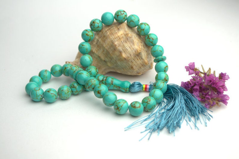 May include: A turquoise blue prayer beads necklace with a tassel. The beads are made of natural stone and have a marbled pattern. The tassel is a light blue color.