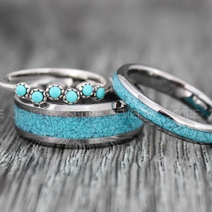 May include: A set of three silver rings with turquoise inlay. The larger rings are a matching pair, and the smaller ring has five turquoise stones.