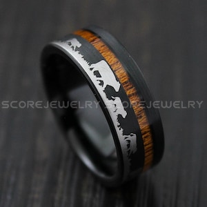 May include: A black tungsten carbide ring with a brown wood inlay and a silver silhouette of a herd of elk.