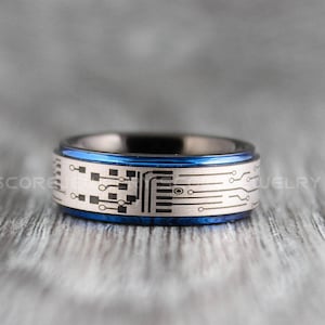 Peut inclure: Une bague en carbure de tungstène bleu et argent avec un motif de circuit imprimé. La bague a un bord biseauté et une finition polie.