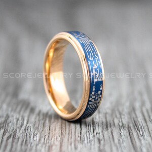 Puede incluir: Un anillo dorado con un diseño de placa de circuito azul. El anillo tiene un acabado pulido y un patrón detallado. El anillo es una joya.