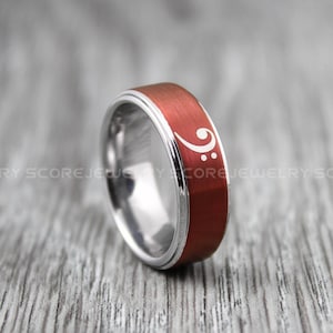 Peut inclure: Une bague en carbure de tungstène rouge et argent avec un symbole de clé de fa grave blanc gravé sur la bande rouge.