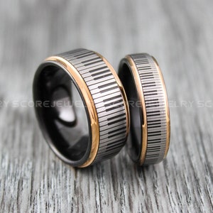 May include: Two black tungsten carbide wedding bands with a piano key design and a gold inlay.