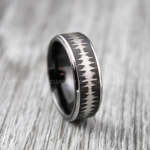 Op de afbeelding: Een zwarte ring van wolfraamcarbide met een zilverkleurig geluidgolfontwerp. De ring heeft een afgeschuinde rand en een gepolijste afwerking.