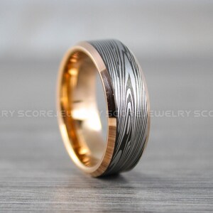 Pode incluir: Um anel de carboneto de tungstênio prateado e ouro rosa com um padrão de grão de madeira. O anel é um estilo clássico de aliança de casamento.