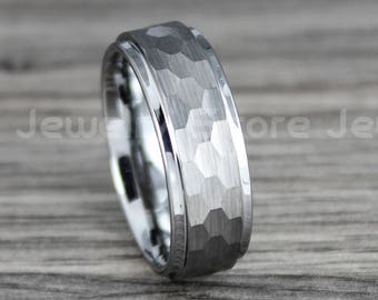 May include: A silver-colored ring with a hammered texture on the outer band and a polished inner band. The ring is set against a gray wooden surface. The words "Score Jewelry" are visible in the background.
