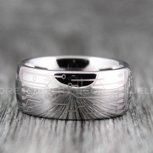 Puede incluir: Un anillo de carburo de tungsteno plateado con un diseño de placa de circuito grabado en la banda.