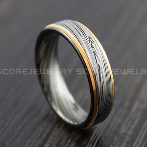 Pode incluir: Uma aliança de casamento prateada e dourada com um padrão e acabamento escovado.
