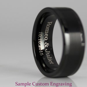 May include: A black wedding band with a beveled edge and a custom engraved inscription that reads "Romeo & Juliet 10.10.2015".