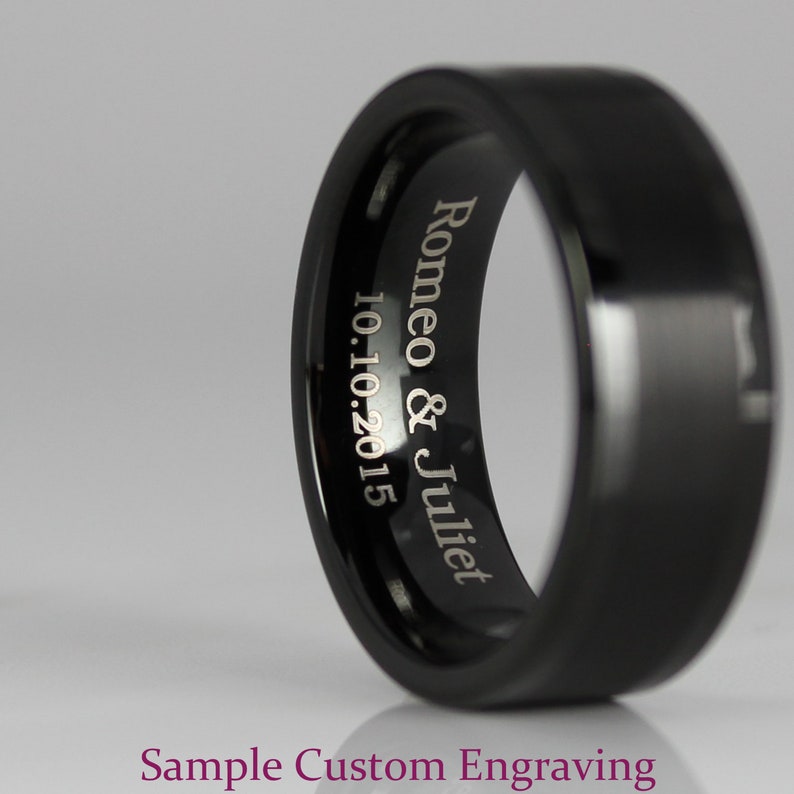 May include: A black wedding band with a beveled edge and a custom engraved inscription that reads "Romeo & Juliet 10.10.2015".