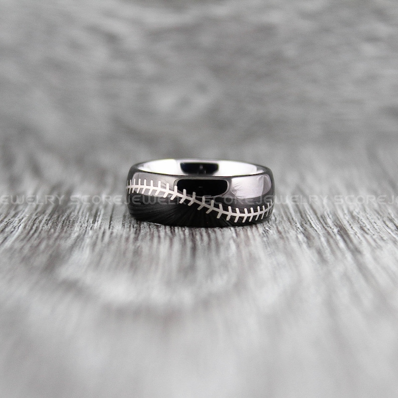 May include: A black tungsten carbide ring with a white baseball stitch design.