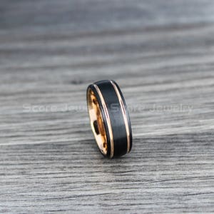May include: A black tungsten carbide ring with two rose gold bands. The ring has a brushed finish.