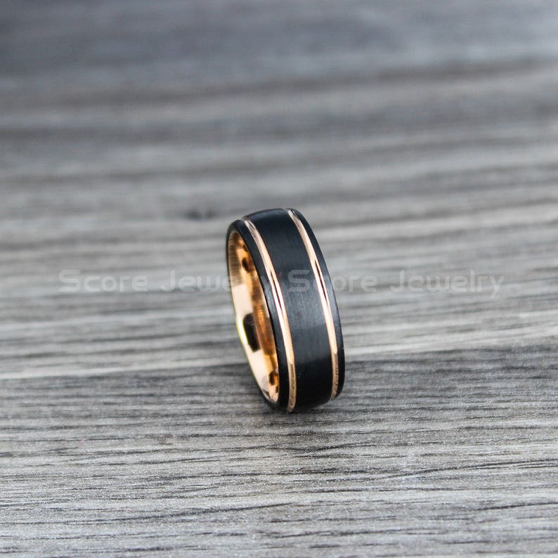 May include: A black tungsten carbide ring with two rose gold bands. The ring has a brushed finish.