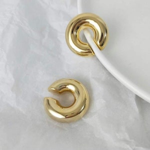 May include: A pair of gold-toned ear cuffs. The cuffs are made of a thick, rounded metal and have a simple, modern design.