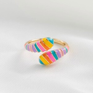 Puede incluir: Un anillo de oro con un diseño de rayas de colores. El anillo está retorcido y tiene una forma única.