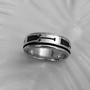 May include: A silver ring with a black inlay design. The design features a stylized arrow shape.