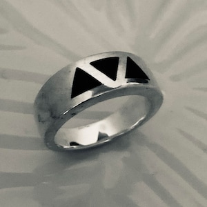May include: A silver ring with a black triangle design. The ring is wide and has a polished finish.