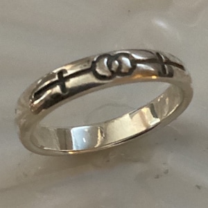 May include: A silver ring with a cross and two intertwined circles engraved on the band.