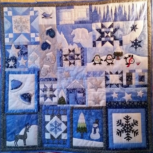 Könnte beinhalten: Eine blaue und weiße Patchwork-Decke mit Winterthema. Die Decke zeigt verschiedene winterliche Motive, darunter Schneeflocken, Pinguine, Fäustlinge, einen Eisbären, ein Reh und einen Schneemann. Die Decke ist aus verschiedenen Stoffen und Texturen gefertigt.