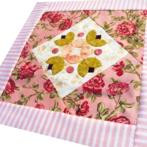 May include: A pink and white striped fabric with a pink floral pattern in the centre. The floral pattern features a central design of overlapping leaves and circles.