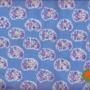 May include: A light blue fabric featuring a repeating pattern of abstract, rounded floral shapes in shades of purple, white, and light blue. A small, stylized orange and green heart-shaped logo is positioned in the bottom right corner.