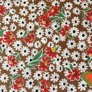 May include: A brown fabric with a repeating pattern of white daisies and red flowers with yellow centers. Green leaves are interspersed throughout the design, creating a vibrant floral print.
