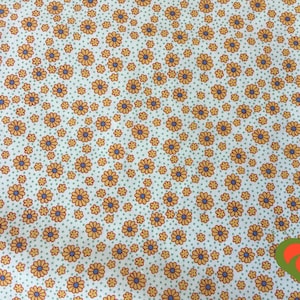 May include: White fabric with a repeating pattern of small orange and blue flowers. The background is a light green color with tiny white dots.