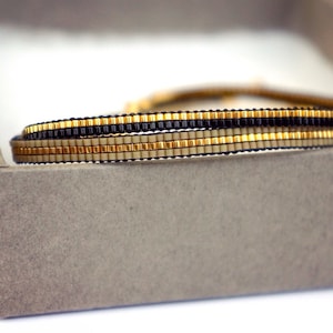 Peut inclure: Un bracelet en perles multi-rangs avec des perles noires, dorées et crème.