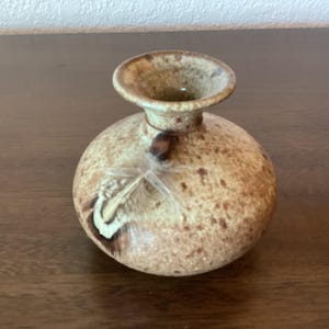 May include: A small, round, speckled brown and cream ceramic vase with a brown feather decoration.