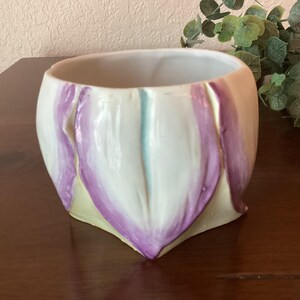 May include: A white ceramic flower pot with purple and yellow painted flower petals.