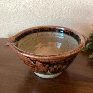 May include: A brown and black ceramic mixing bowl with a speckled glaze and a pouring spout. The bowl has a white rim and a white base.