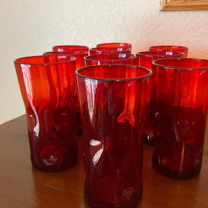 May include: Set of ten red glass tumblers with a textured design. The glasses are arranged in three rows on a wooden surface.