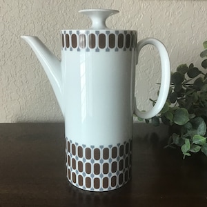 May include: White ceramic coffee pot with a brown and gray geometric pattern. The pot has a lid and a handle.