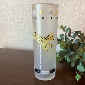 May include: A frosted glass tumbler with a cheetah on a carousel design. The cheetah is yellow with black spots and the carousel is white with black and white details.
