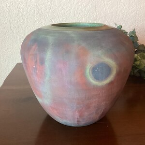 May include: A large, round, ceramic vase with a green rim. The vase has a mottled, abstract design in shades of red, orange, green, and blue.