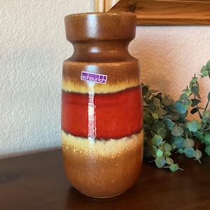 May include: A brown ceramic vase with a red, white, and yellow glaze. The vase has a label that says "scheurich".