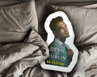 May include: A white pillow with a book cover design featuring a man with dark hair and a white shirt. The book cover text reads "Devil of Dublin" and "BB Easton".