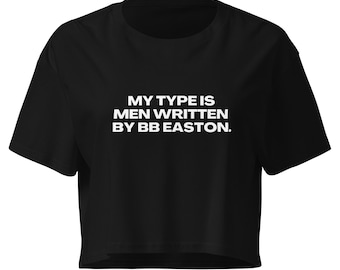 May include: A black short-sleeved crop top featuring the white text MY TYPE IS MEN WRITTEN BY BB EASTON. centered on the chest. The garment has a crew neckline and a straight hemline, providing a simple and clean look for this casual piece of clothing.
