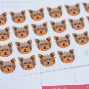 May include: A sheet of stickers featuring a repeated pattern of brown and tan Yorkshire Terrier dog faces. The stickers are on a white background and have the text "Bella Rose" in blue and white.