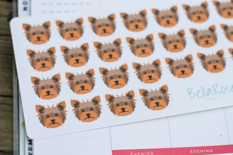 May include: A sheet of stickers featuring a repeated pattern of brown and tan Yorkshire Terrier dog faces. The stickers are on a white background and have the text "Bella Rose" in blue and white.
