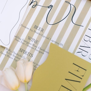 May include: A yellow card with the word "FIVE" printed in black letters. The card is on a white and brown striped surface with a handwritten menu listing beer, wine, and spirits.