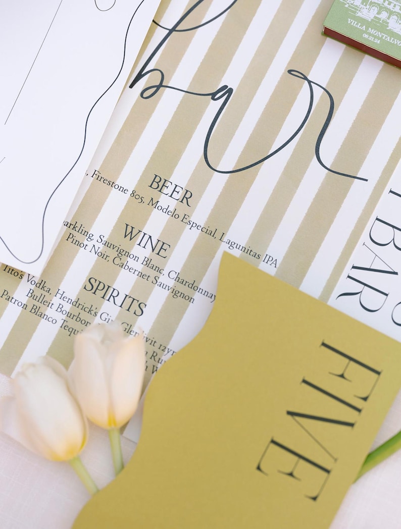 May include: A yellow card with the word "FIVE" printed in black letters. The card is on a white and brown striped surface with a handwritten menu listing beer, wine, and spirits.