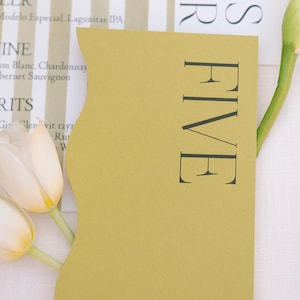 May include: A mustard yellow table number card with the word "FIVE" printed in black.