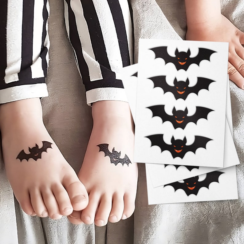 May include: Four black bat temporary tattoos with orange eyes on a white sheet of paper. A child's feet are shown with two of the tattoos applied.