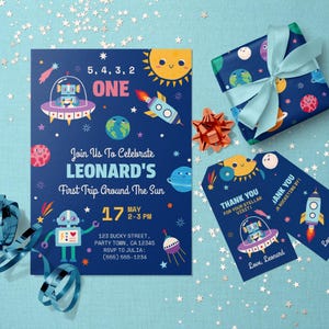 May include: A blue and white invitation for a first birthday party with a space theme. The invitation features a robot in a spaceship, planets, stars, and the text "Join us to celebrate Leonard's First Trip Around the Sun".