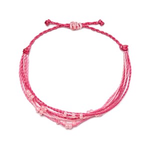 Puede incluir: Un brazalete trenzado de color rosa y blanco con pequeñas cuentas rosas.