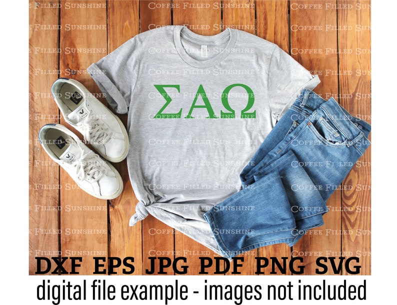 May include: A gray t-shirt with the Greek letters "&Sigma;&Alpha;&Omega;" in green on the front. The t-shirt is laid out on a wooden surface with a pair of white sneakers and blue jeans.