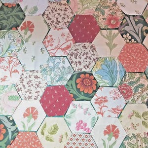 May include: A close-up of a patchwork design composed of hexagonal fabric pieces. The fabrics display floral patterns in red, pink, green, blue, and cream. The arrangement creates a textured surface, ideal for quilting or craft projects.