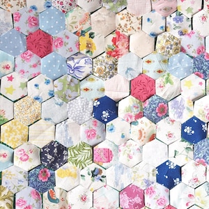 May include: A close-up of a patchwork quilt made from many hexagonal fabric pieces. The quilt displays a variety of floral patterns in shades of pink, blue, yellow, and white. The quilt's design is a mix of vintage and modern styles.