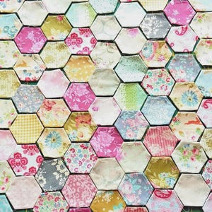 May include: Close-up of a patchwork quilt made from many hexagonal fabric pieces. The quilt displays a variety of floral and patterned fabrics in pink, green, yellow, and blue, creating a colourful and textured design.